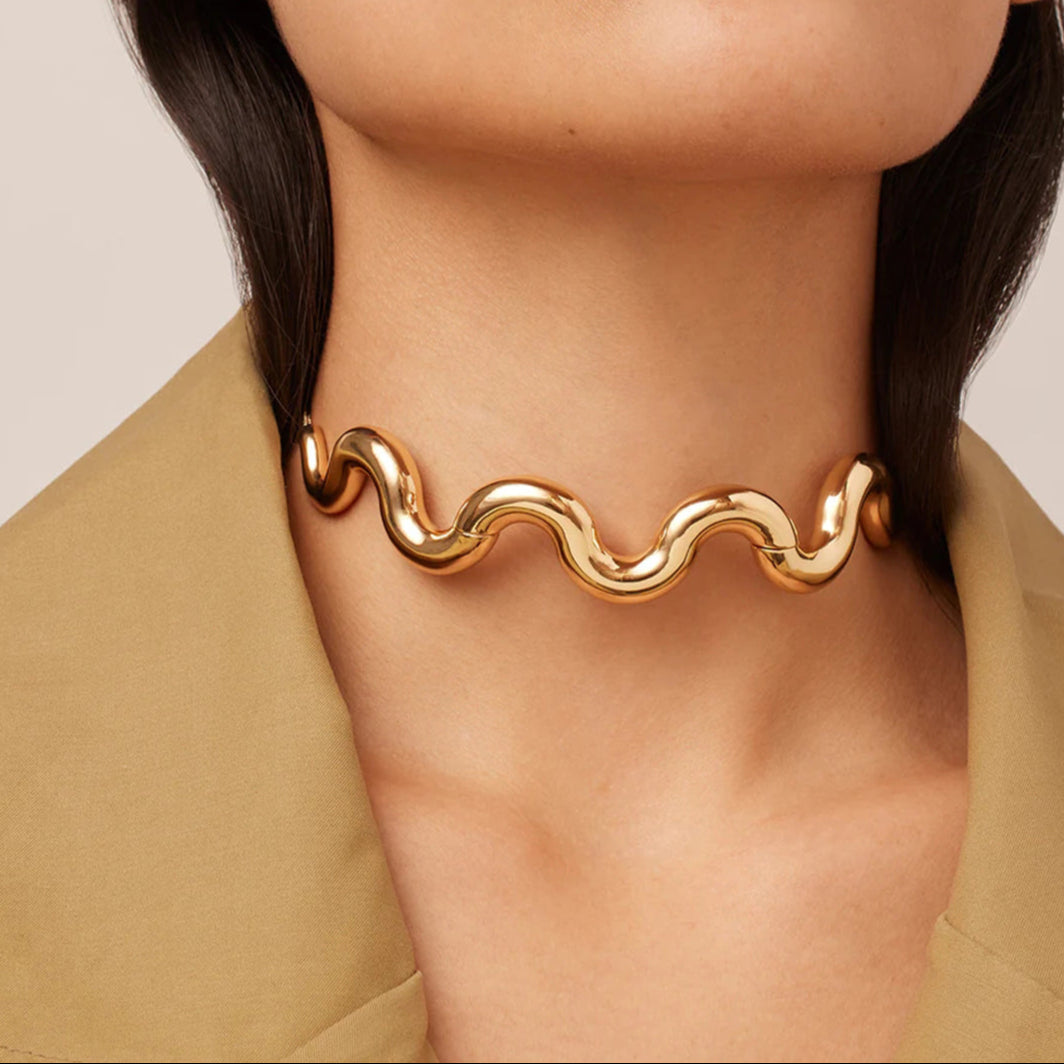 Gold wavy necklace worn by a person with a neutral background