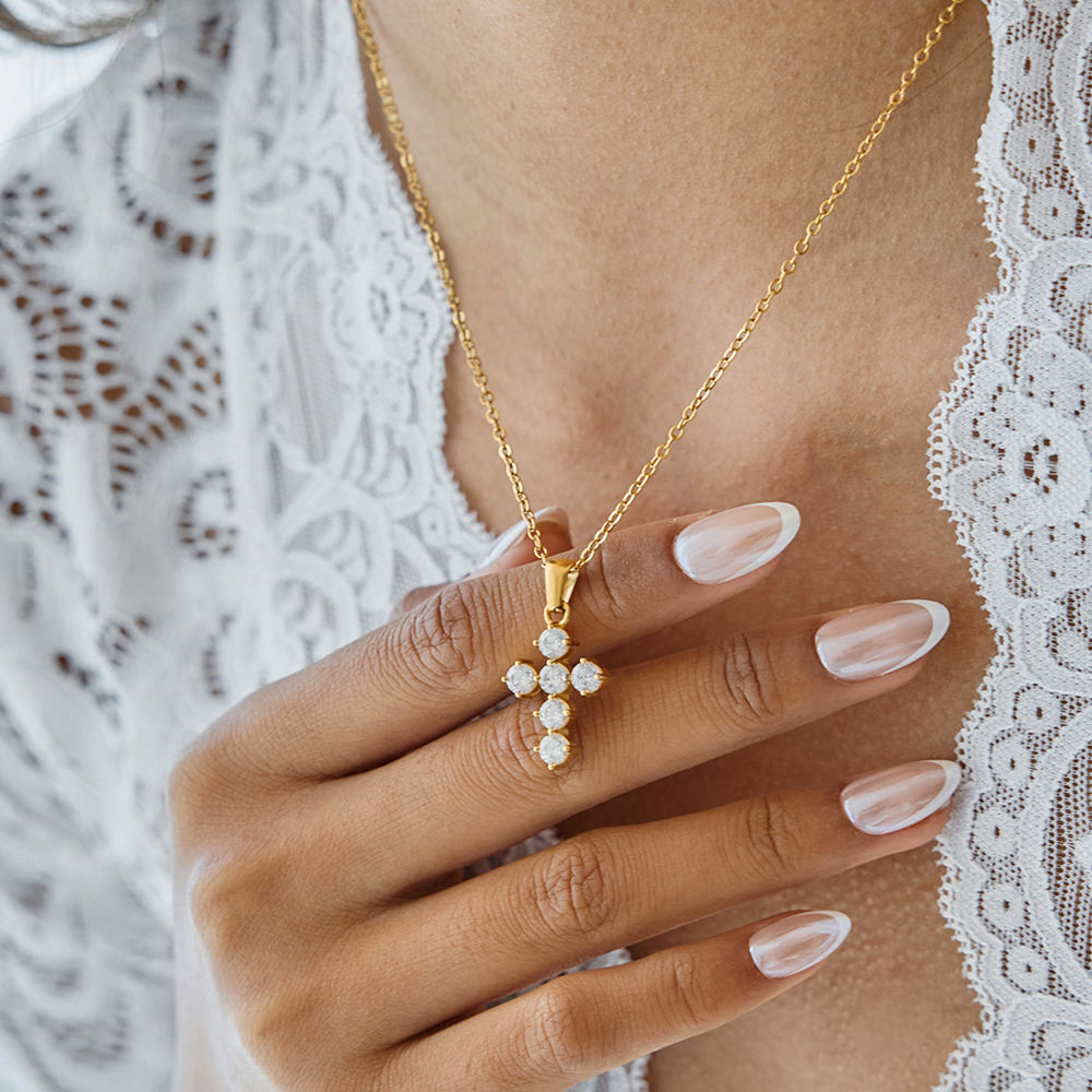 Gold necklace with a cross pendant worn by a person against a white lace background