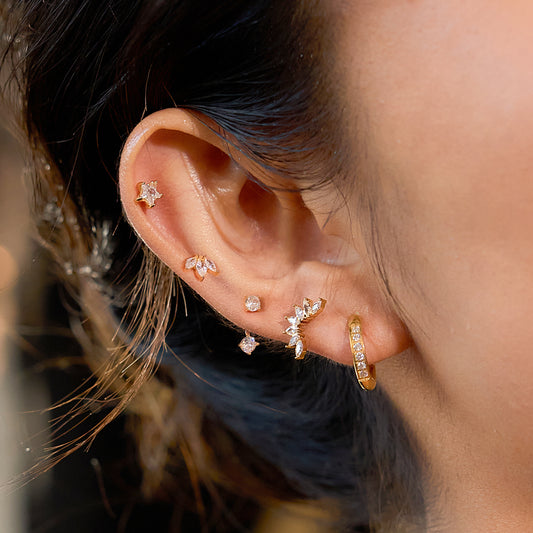 Close-up of an ear wearing multiple gold and diamond earrings with a blurred background.