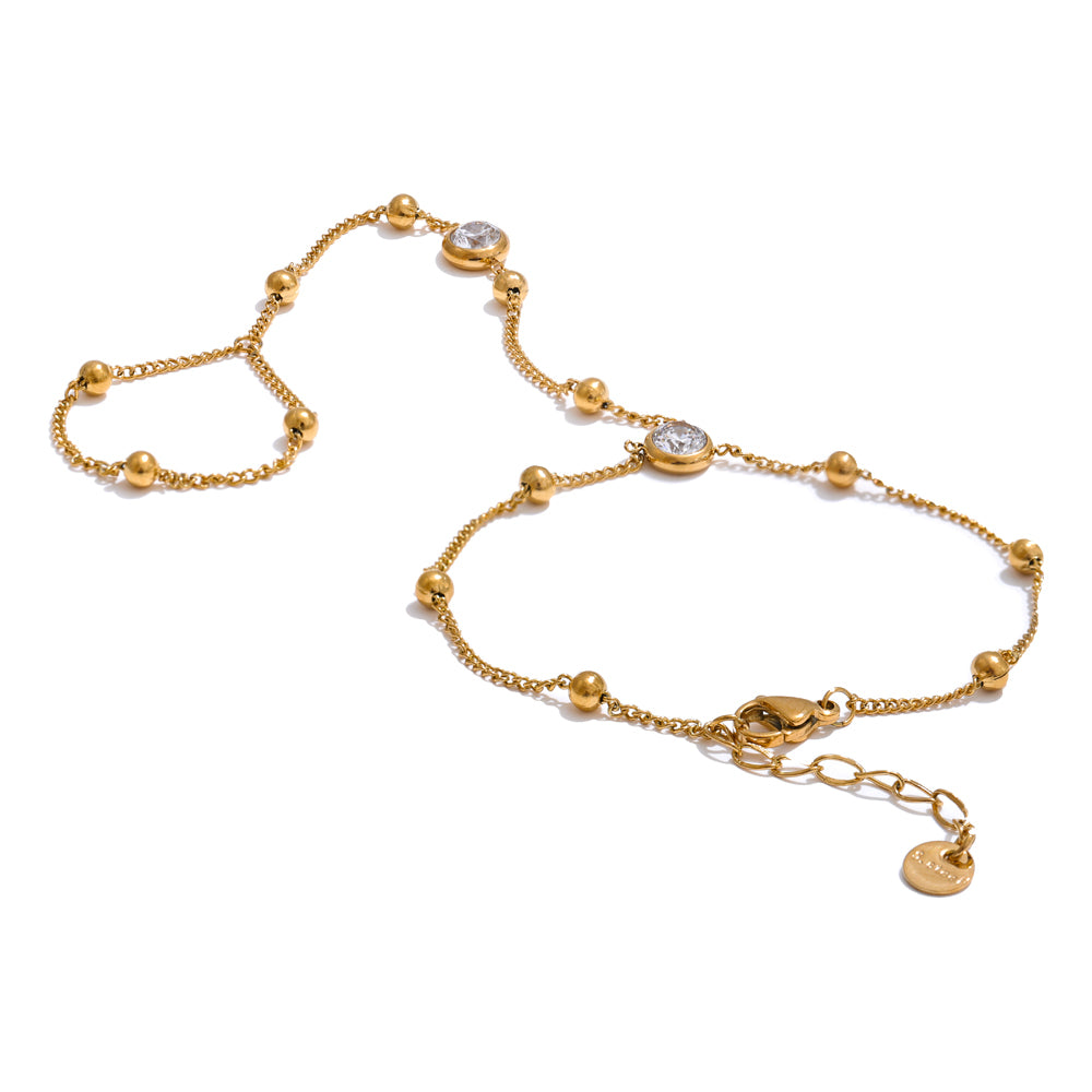 Adorned 18K gold-plated hand chain bracelet featuring delicate gold links, round gold beads, two clear zircon stones, a finger loop, and an adjustable lobster clasp on a white background.