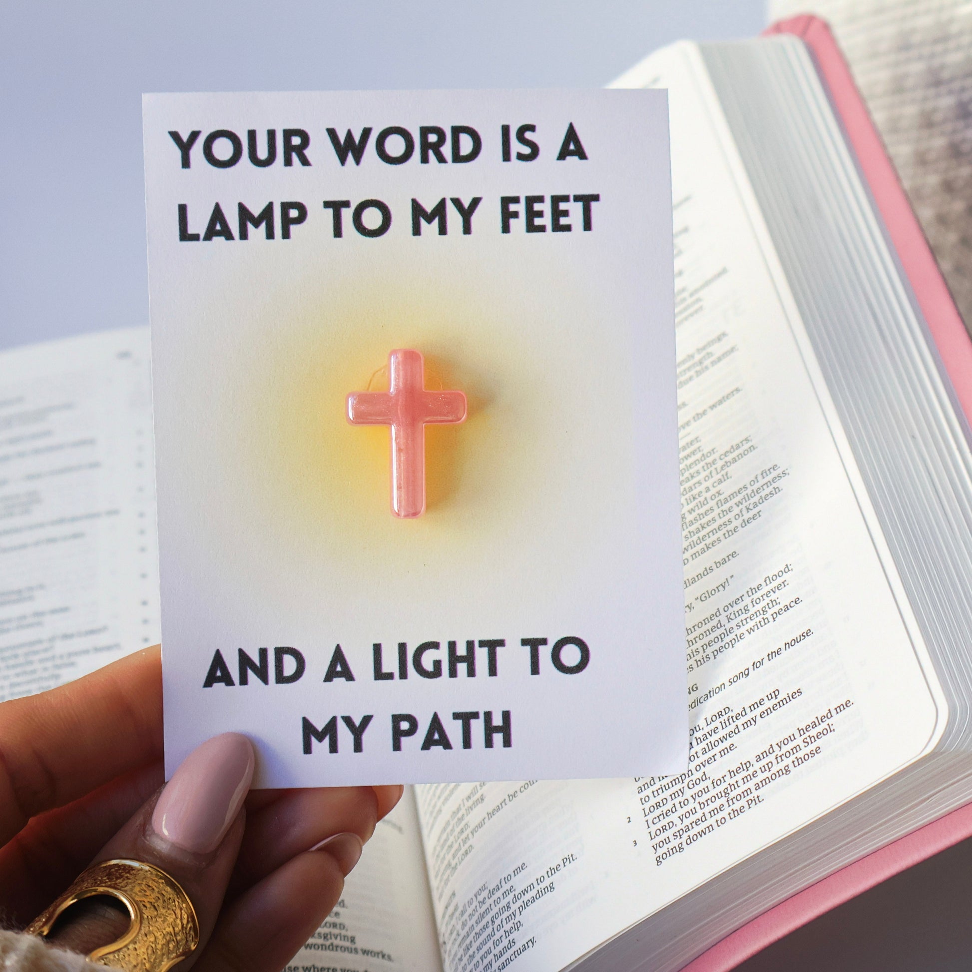 Open Bible with a card overlay featuring a cross and text, held by a hand.