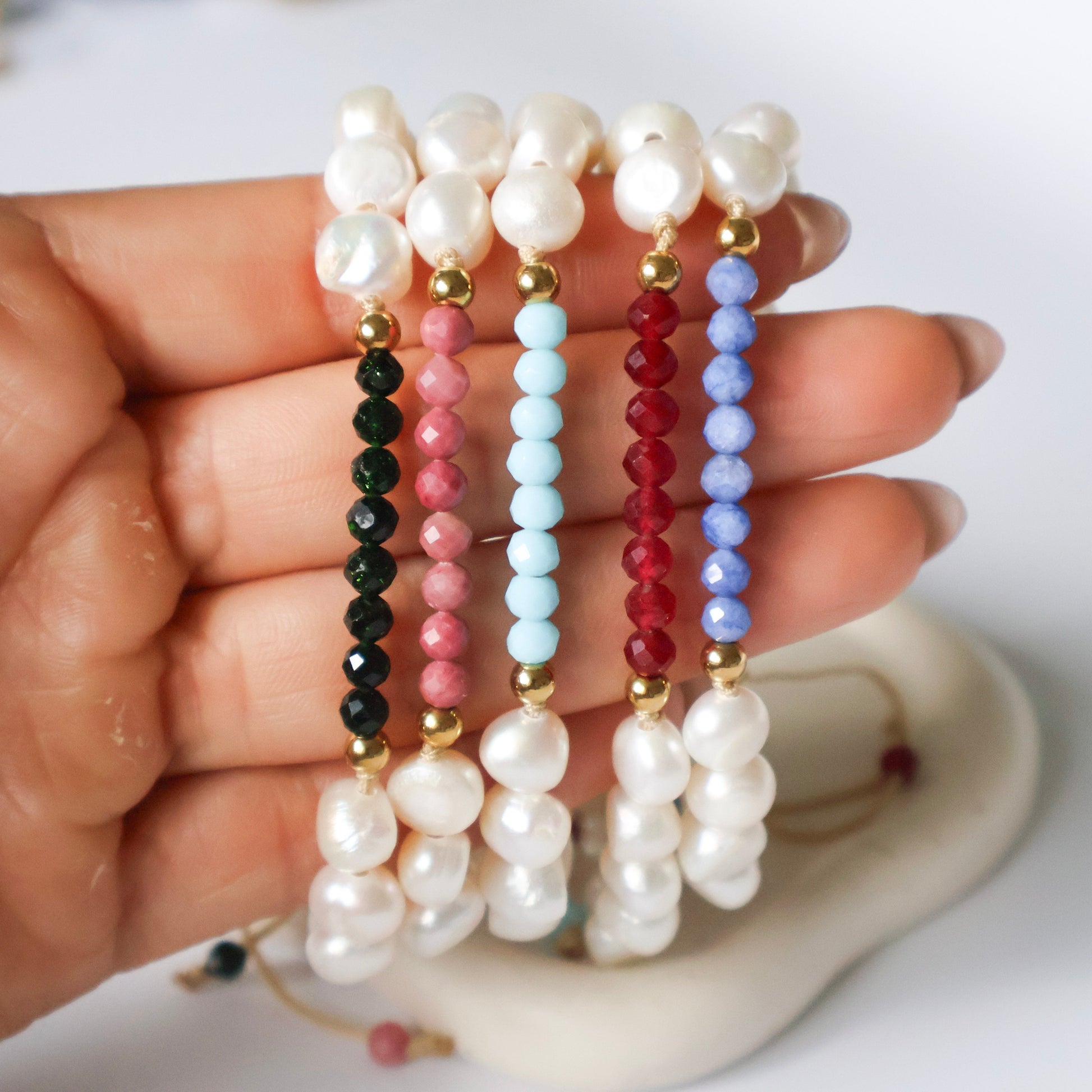Hand holding a set of pearl and beaded bracelets on a white background