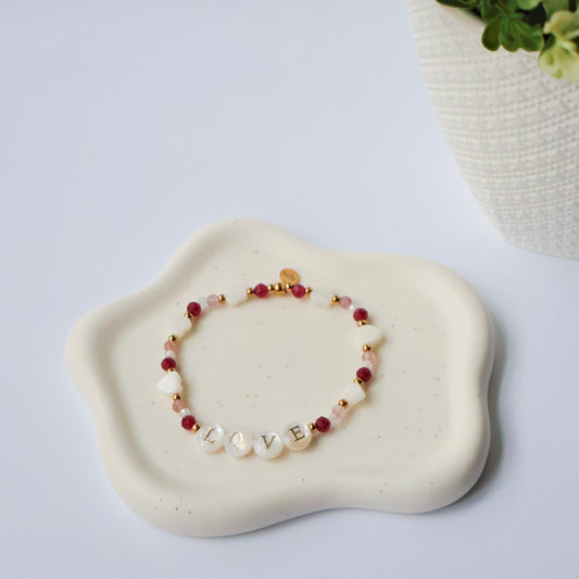 Bracelet with the word Love, red and white beads on a white stone surface with a plant in the background
