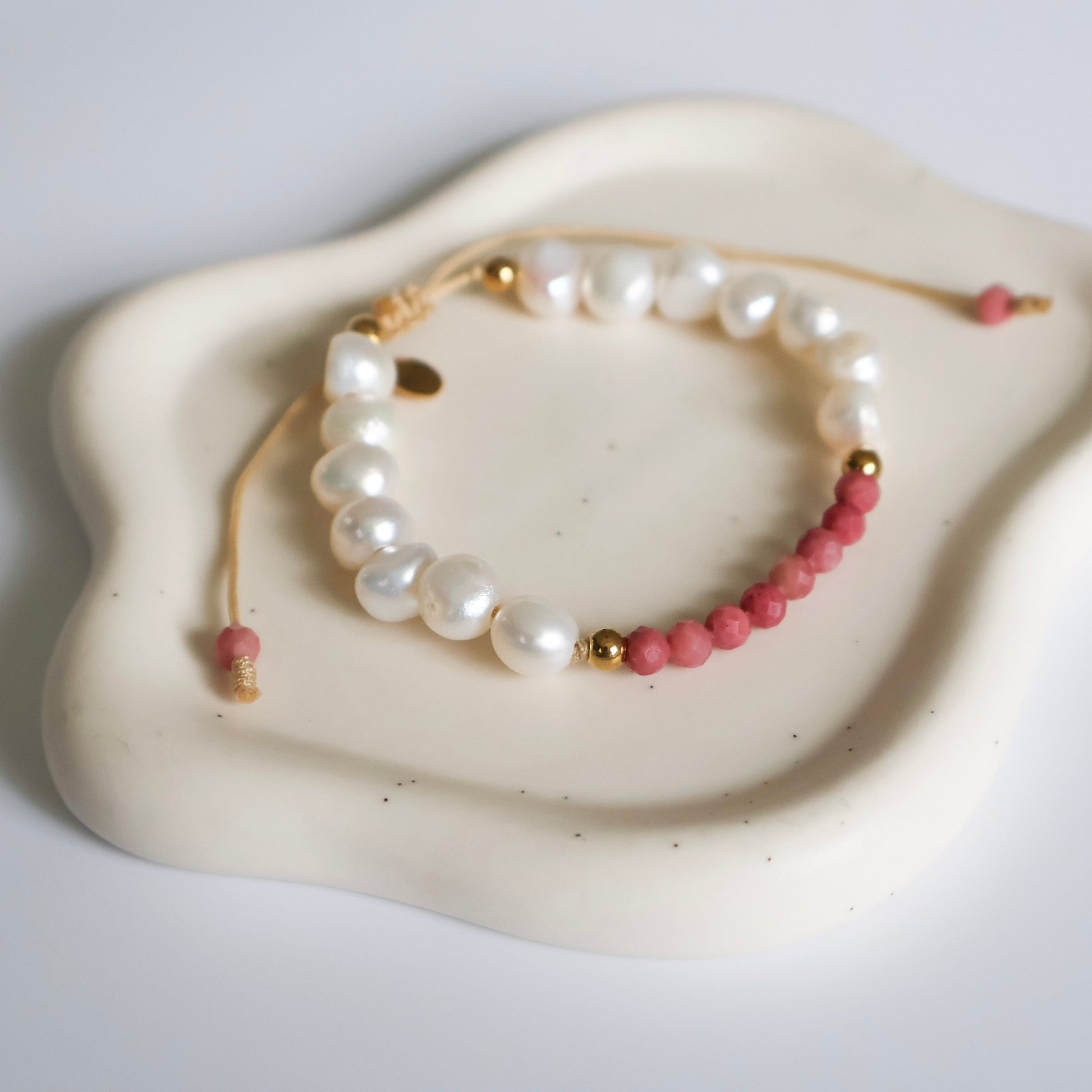 Pearl and pink bead bracelet on a white dish with a light gray background