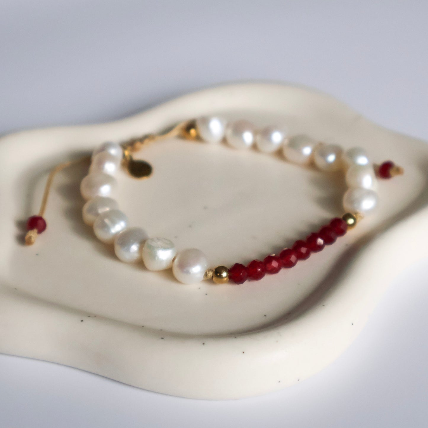 Pearl and red bead bracelet on a white dish with a gray background