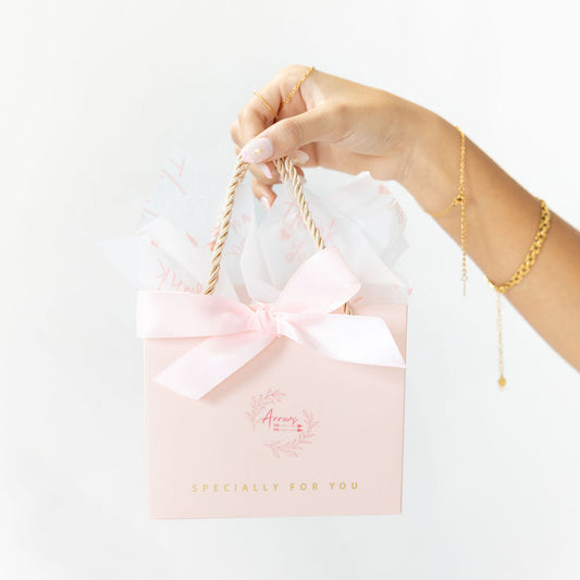 Hand holding a pink gift bag with a white bow against a white background