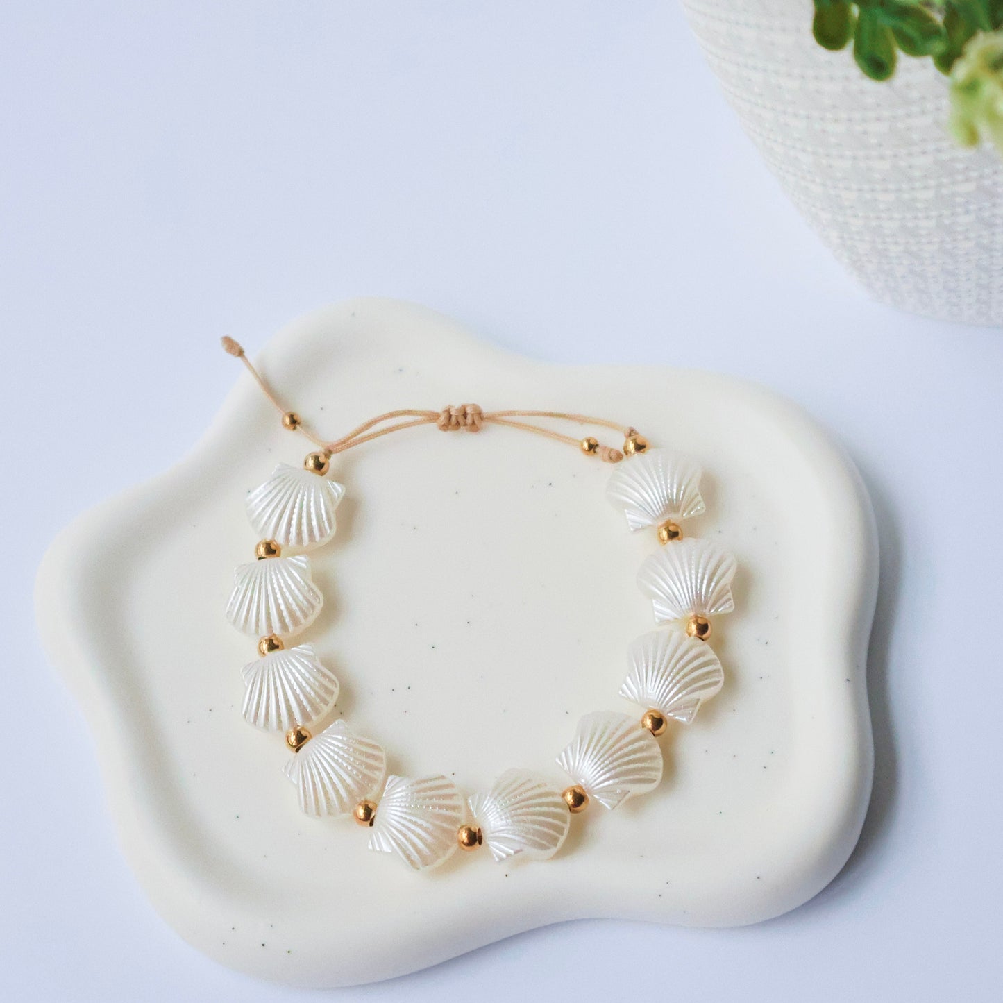 Bracelet with shell-like beads on a white stone surface with a plant in the background